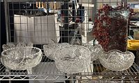 Wide view of three cut crystal bowls on metal shelf with one glass vase containing red berries to far right.