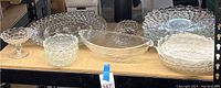 Full view of glass and crystal serviceware collection including large platters and various sized bowls with different patterns and edges on a table.