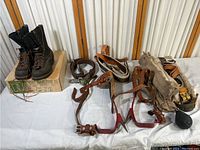 Collection of horse tack items including multiple leather bridles with metal bits, reins, a sheepskin-lined saddle pad, and several leather belts.