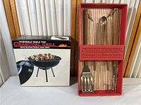 Full view of portable table top charcoal grill box next to charcoal companion professional chef barbecue tool set in original packaging.