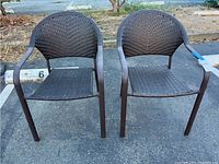Two brown faux wicker outdoor chairs with metal frames, placed on pavement, showing signs of sun fading and aging.