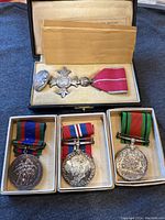 Group shot showing all four medals in original boxes: MBE cross and three campaign medals.