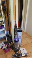 Dyson DC66 upright vacuum with clear bin and purple cyclone next to V8 Absolute box and floor head
