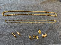 All items laid out on fabric background: two necklaces at top, earrings and charms below