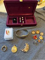 Overview of jewelry on display including case, ring, bangle, brooch, pendants, charms, earrings, pins