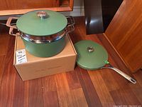 Overview of 12" fry pan with lid beside 10" saucepan with strainer insert and lid on box