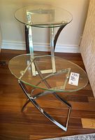 Two side tables with glass tops and metal bases, one taller with rectangular base, the other shorter with curved X-shaped base.