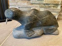Side view of soap stone walrus carving showing tusks and rock base.