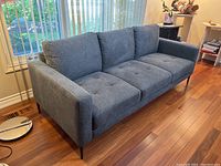 Front-left angled view of grey sofa on hardwood floor by window
