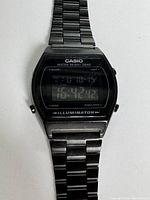 Close-up of Casio LCD digital watch face and part of metal band. Shows digital display, buttons, and branding.