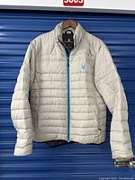 Front view of the light gray men’s Spyder down jacket with blue zipper and spider logo.