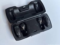 Opened charging case showing pair of black Bose wireless earbuds in charging slots.