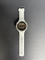 White Suunto D4i dive computer watch laid flat on a black background, showing the time 10:34 and date on the digital display.