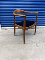 Full view of vintage mid century teak armchair showing curved armrest and black seat against blue door
