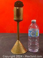 Antique brass whale oil lamp next to a water bottle for size reference, showing tall slender stem and conical base.