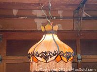 Front view of antique slag glass chandelier showing cream white and amber slag glass with ornate metal filigree and fabric fringe bottom edge