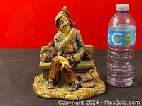 Front view of the hand painted ceramic figurine showing the man sitting on the bench holding a book next to a dog, with a water bottle for size comparison.