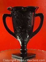 Front view of black glass vase with two handles and ornate floral relief on the body