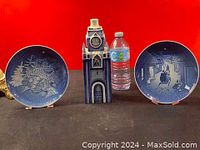 Blue and white Christmas church ceramic figurine with two decorative blue and white Christmas plates and water bottle for size reference on display against red background.