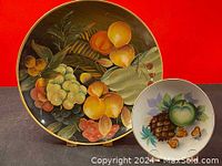 Full view of two decorative fruit plates against a red background, showing colorful painted fruit.