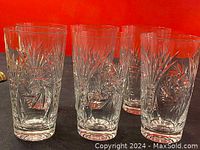 Front view showing six clear crystal cut glasses with starburst and geometric cut patterns against an orange background.