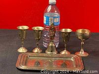 Five silver plated goblets, one silver plated bell with figurine handle, and rectangular silver plated serving tray next to a water bottle for scale