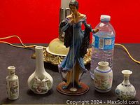 Photo of four small vintage ceramic vases/mugs with Asian-inspired paintings and a porcelain figurine of a woman playing the flute, placed beside a water bottle for scale.