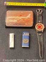 Overview of watch, two lighters, and airplane paperweight with measuring tape for scale