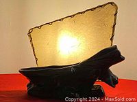 Side view of black ceramic lamp base with lit triangular lampshade showing texture and size reference on red background