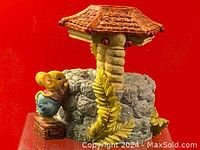 Side view of music box showing mouse next to stone well and yellow leaves on a red background.