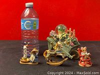 Lot items with water bottle for scale, showing two musical animal figurines and decorative wooden cart with flowers and snow globe