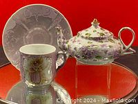 Purple floral teapot with gold accents on handle and lid, displayed with matching cup and saucer