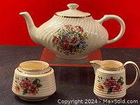 Porcelain teapot with matching creamer and sugar bowl shown from side with floral design and gold accents.