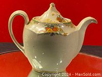Side view of ceramic teapot showing hand painted floral design and gold trim