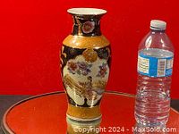 Full front view of the vase showing floral and bird motifs beside a water bottle for scale.