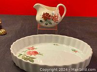 Photo showing the porcelain creamer jug with red and pink rose floral design on a black background with red backdrop.