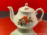 Front view showing the teapot spout and floral design with red poinsettia and white flowers with green holly leaves.