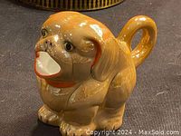 Close-up photo of one ceramic dog-shaped mug, brown with detailed facial features and curled tail handle.