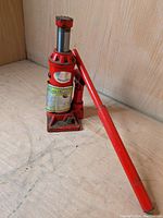 Full view of red 3 tonne hydraulic jack showing base, body, handle, piston, and labels.