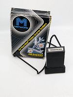 Photo showing Atari M Network Air Raiders game box and game cartridge with attached cord, box shows visible wear and damage.