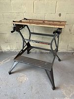 Front view of Black & Decker Workmate showing metal frame, wooden adjustable clamping top, and footrest platform