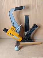 Bostitch floor nailer with wooden mallet and black pry bar displayed on wooden surface.