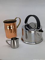 Photo showing the three items together: Bodum Osiris stainless steel tea kettle with handle, Oneida stainless steel creamer, and copper pitcher with brass handle.