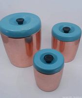 Set of three copper kitchen storage containers of varying sizes with blue lids and black knobs, displayed together.