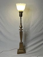 Full view of entire table lamp lit, showing metal body and frosted glass shade.