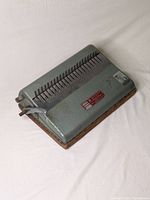 Front angled view showing metal body, comb binding teeth, and wooden base with signs of surface wear.