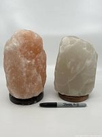 Two large Himalayan salt lamps, pink and white, standing side by side with a black marker for scale under the pink lamp