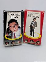 Front view of two VHS tapes in cardboard slip covers featuring Rowan Atkinson as Mr. Bean. One titled 'Unseen Bean' from 1991, the other 'The Amazing Adventures of Mr. Bean' from 1995.