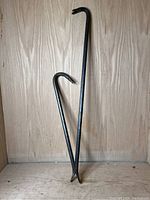 Two and three prybars set shown standing against a wooden background, clear details of claw ends and tapered bars visible.