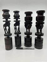 Full set of four dark wood carved candlestick holders with animal motifs shown alongside marker for scale.